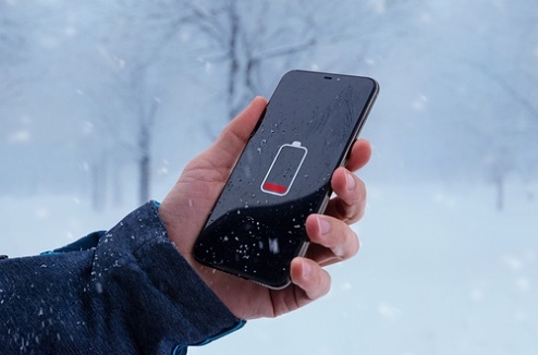Un homme tient un smartphone déchargé dans un paysage enneigé