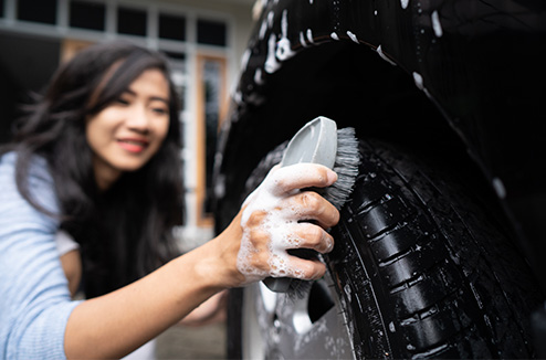 Laver sa voiture est essentiel pour garder un environnement sain ! Une jeune femme passant une éponge sur une voiture noire savonnée