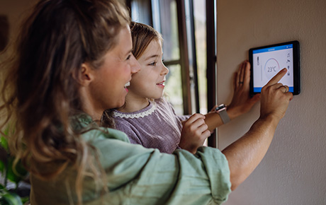 Une femme et sa fille appuyant sur l'écran d'un thermostat connecté accroché au mur