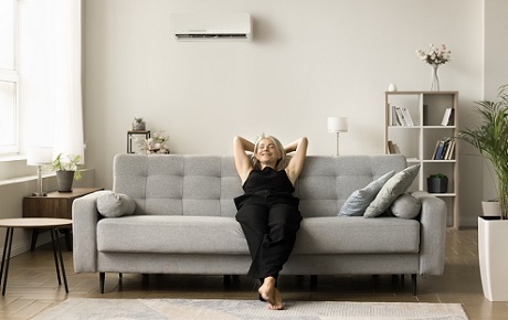 Jeune femme profite de la climatisation assise sur un canapé dans son salon