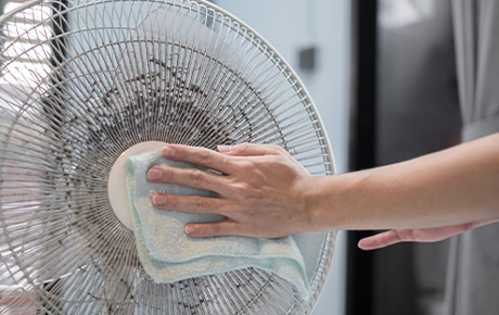 Une personne qui nettoie un ventilateur sur pied plein de poussières