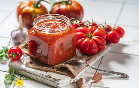 Un bocal de sauce rouge entouré de tomates sur un plan de travail
