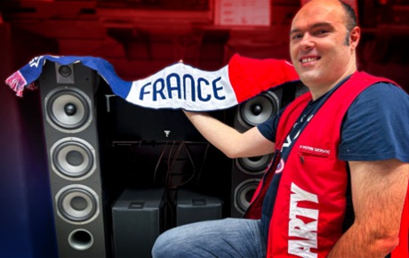 Un vendeur Darty tient une echarpe made in France au dessus d'une paire d'enceintes colonnes