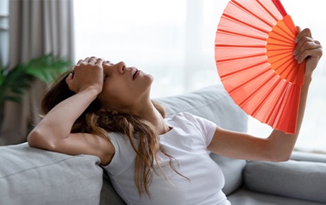 Une femme assise sur son canapé s'évente avec un éventail orange
