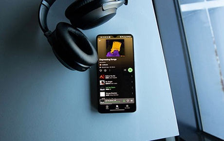 Un casque filaire est branché sur un smartphone affichant une liste de lecture audio