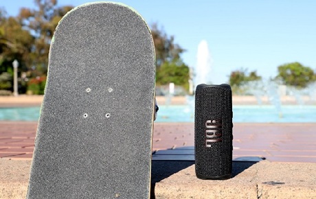 Une enceinte JBL est posée au sol près d'une piscine et à côté d'un skate 