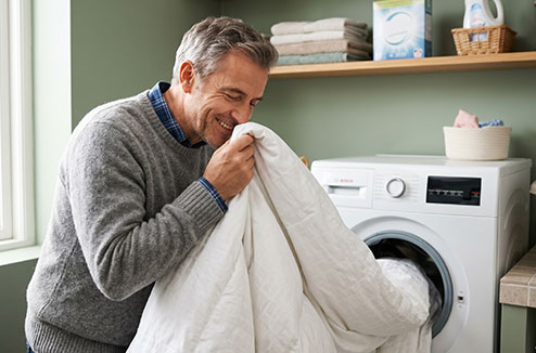 Une homme respire le parfum d'ue couette qui sort de la machine à laver