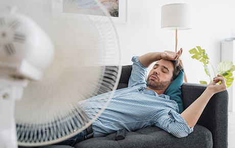 Un homme couché sur son canapé en face d'un ventilateur