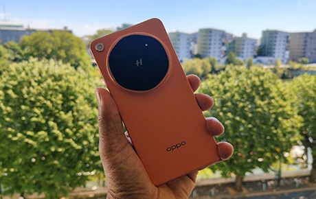Un homme tient dans sa main un Oppo Find X9 Ultra avec des arbres et des bâtiments en arrière-plan
