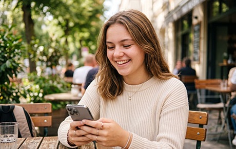 Une jeune fille assise en en extérieur utilise son smartphone 