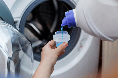 Une personne verse de la lessive liquide dans sa machine à laver