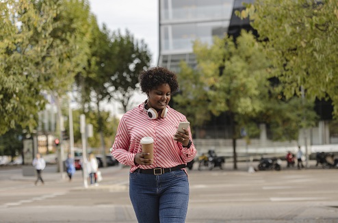 Une femme noire marche dans la rue en regardant son smartphone