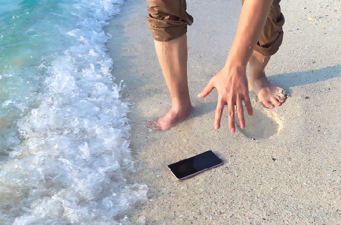 Homme se penche pour ramasser son smartphone avant qu'une vague le touche