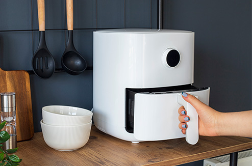 Une main de femme ouvrant un airfryer à 1 tiroir blanc