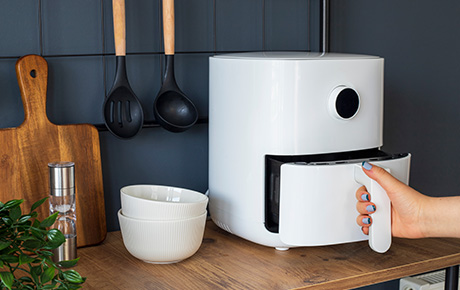 Une main de femme tirant le tiroir d'un airfryer blanc dans une cuisine