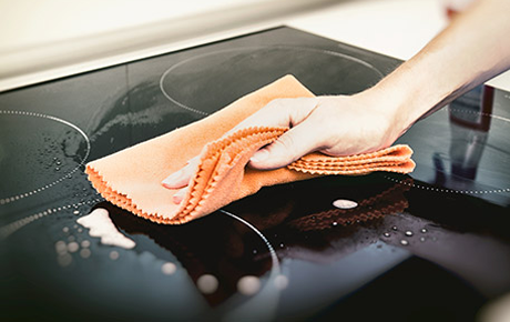 Une main nettoyant une plaque vitrocéramique noire avec un chiffon orange