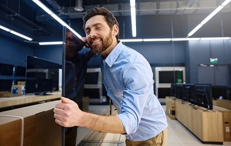 Un homme barbu en chemise embrasse une TV dans le rayon dédié d'un magasin